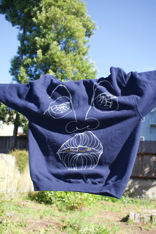 Navy blue hoodie with white abstract designs on a background of trees and a building.